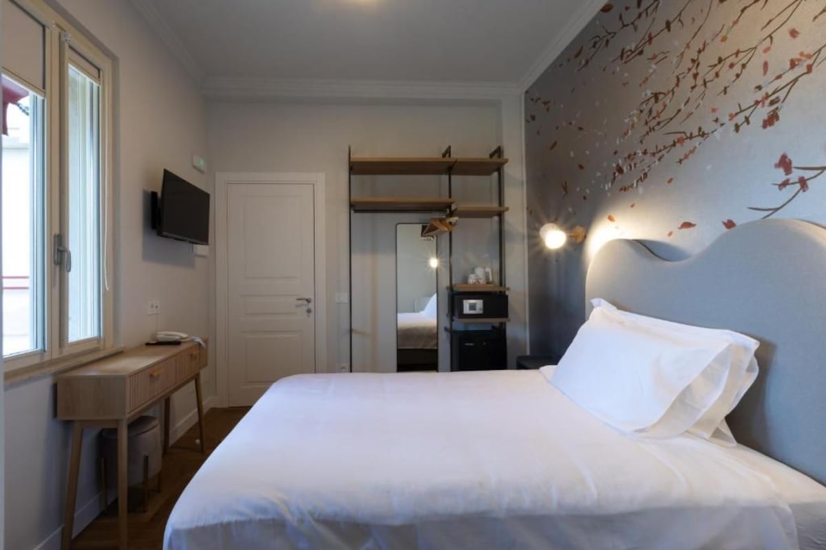 A hotel room with a bed, a desk, a television, and a wall-mounted shelf.