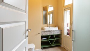 Un baño con inodoro blanco, lavamanos con espejo superior y estante verde.