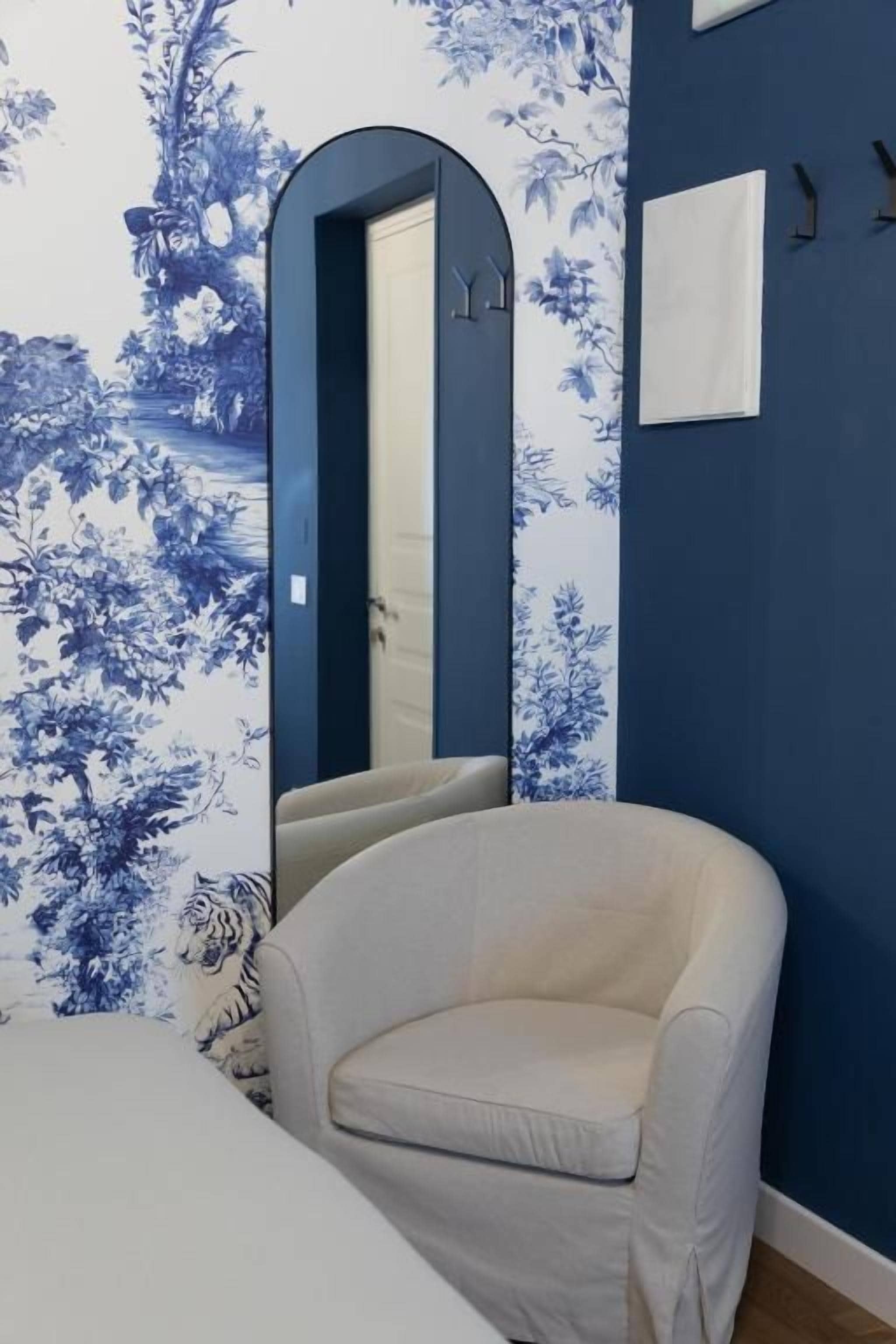 Une pièce avec un mur bleu, une chaise blanche, un lit et un miroir.