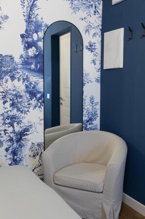 A room with a blue wall, a white chair, a bed, and a mirror.