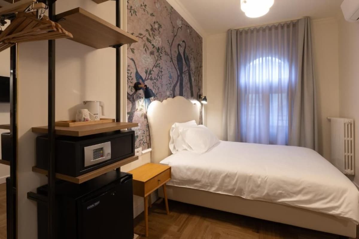 A bedroom with a bed, a desk with a computer, a radiator, and a wall with a bird mural.
