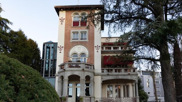 Un edificio de varios pisos con entrada central, balcones y una escalera que conduce a la entrada.