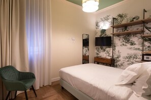 Makuuhuoneessa on sänky, tuoli, televisio ja seinälle kiinnitetty hylly.