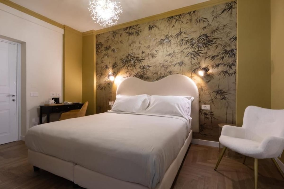 A hotel room with a bed, a desk, a chair, and a wall with a bamboo pattern.