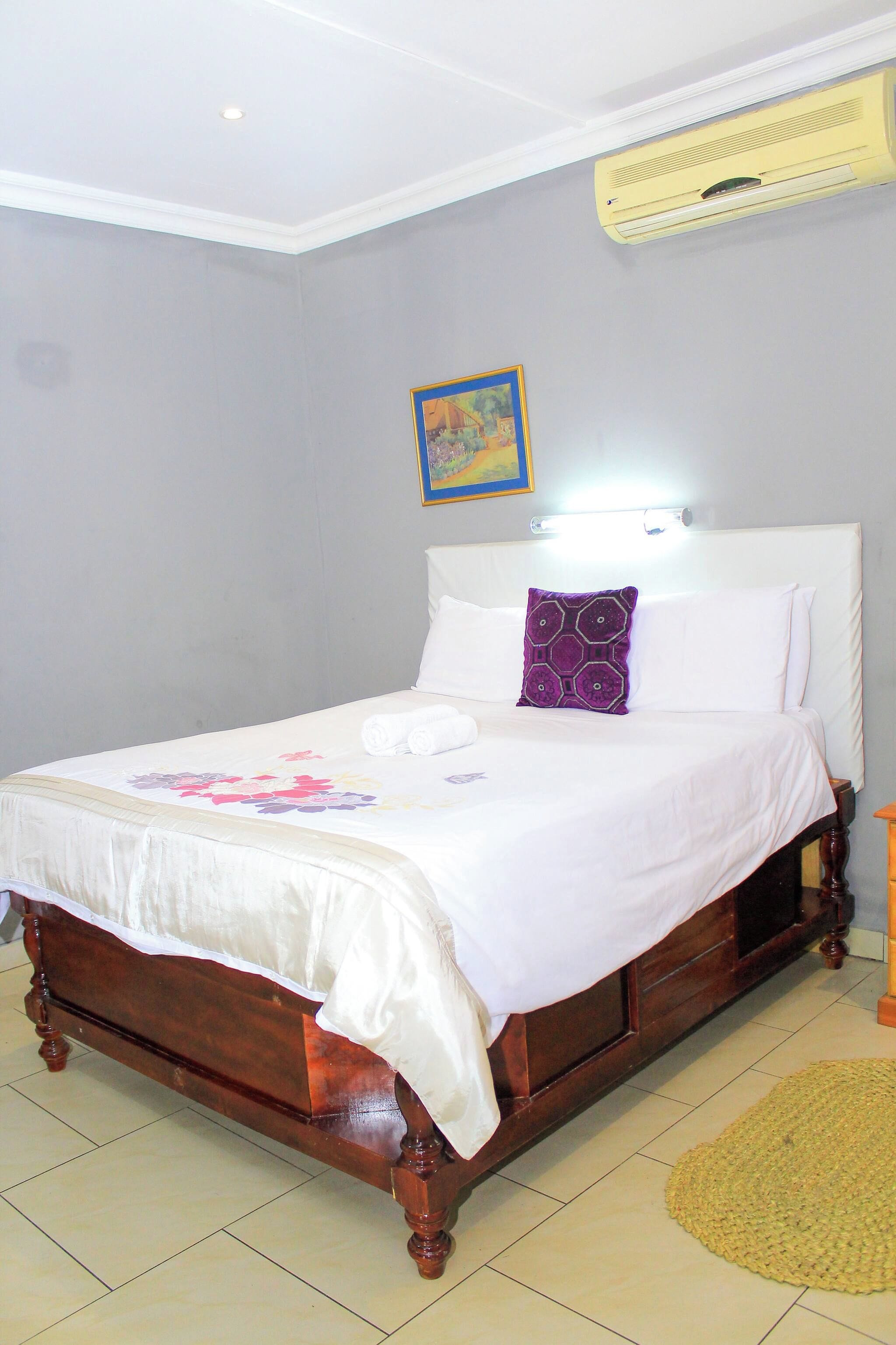A neatly made bed with a white bedspread and a purple pillow, a wooden headboard, and a small rug on the floor.