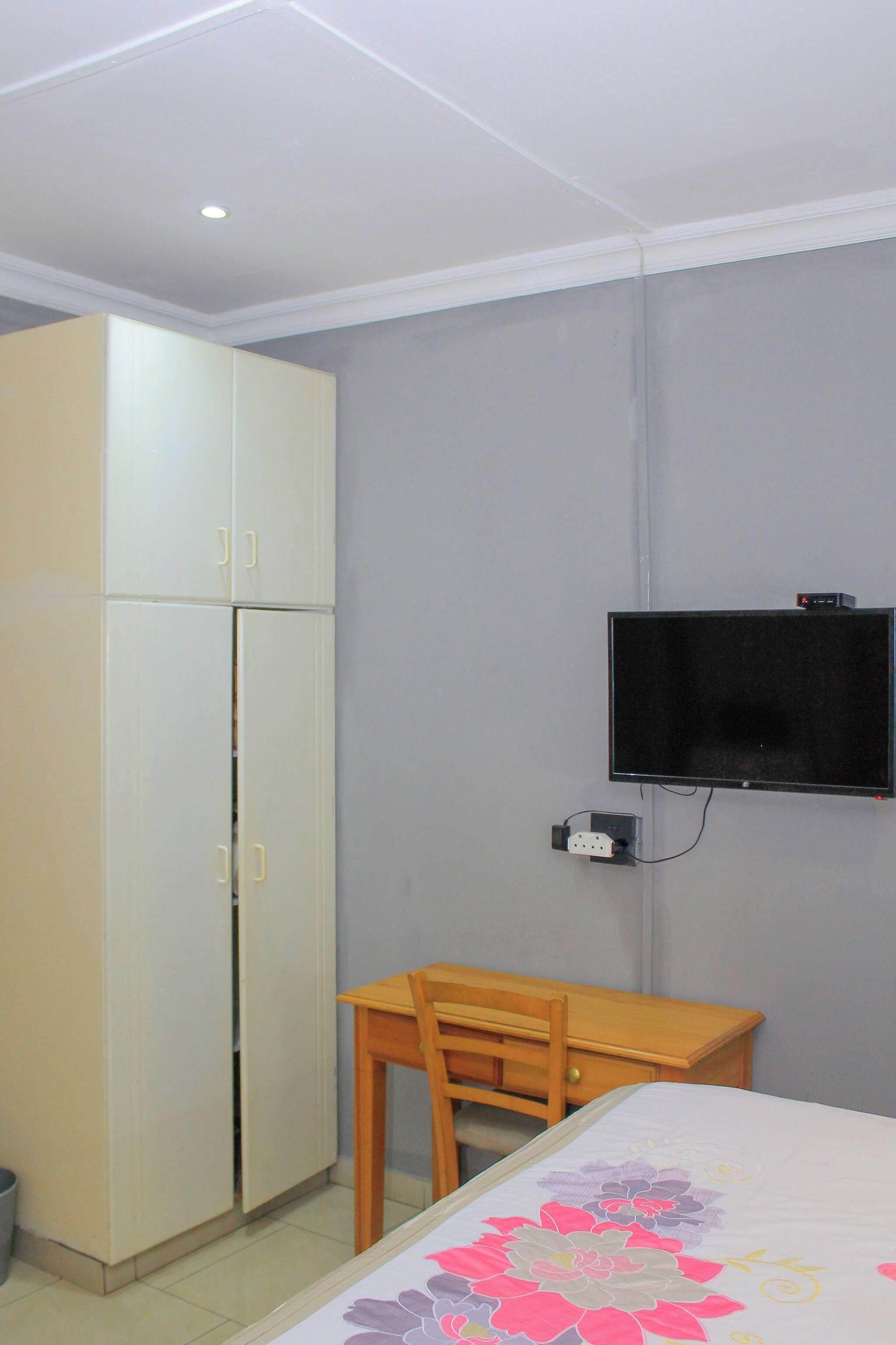 Ein Zimmer mit einem Bett, einem Schreibtisch, einem an der Wand befestigten Fernseher und einem Kleiderschrank.