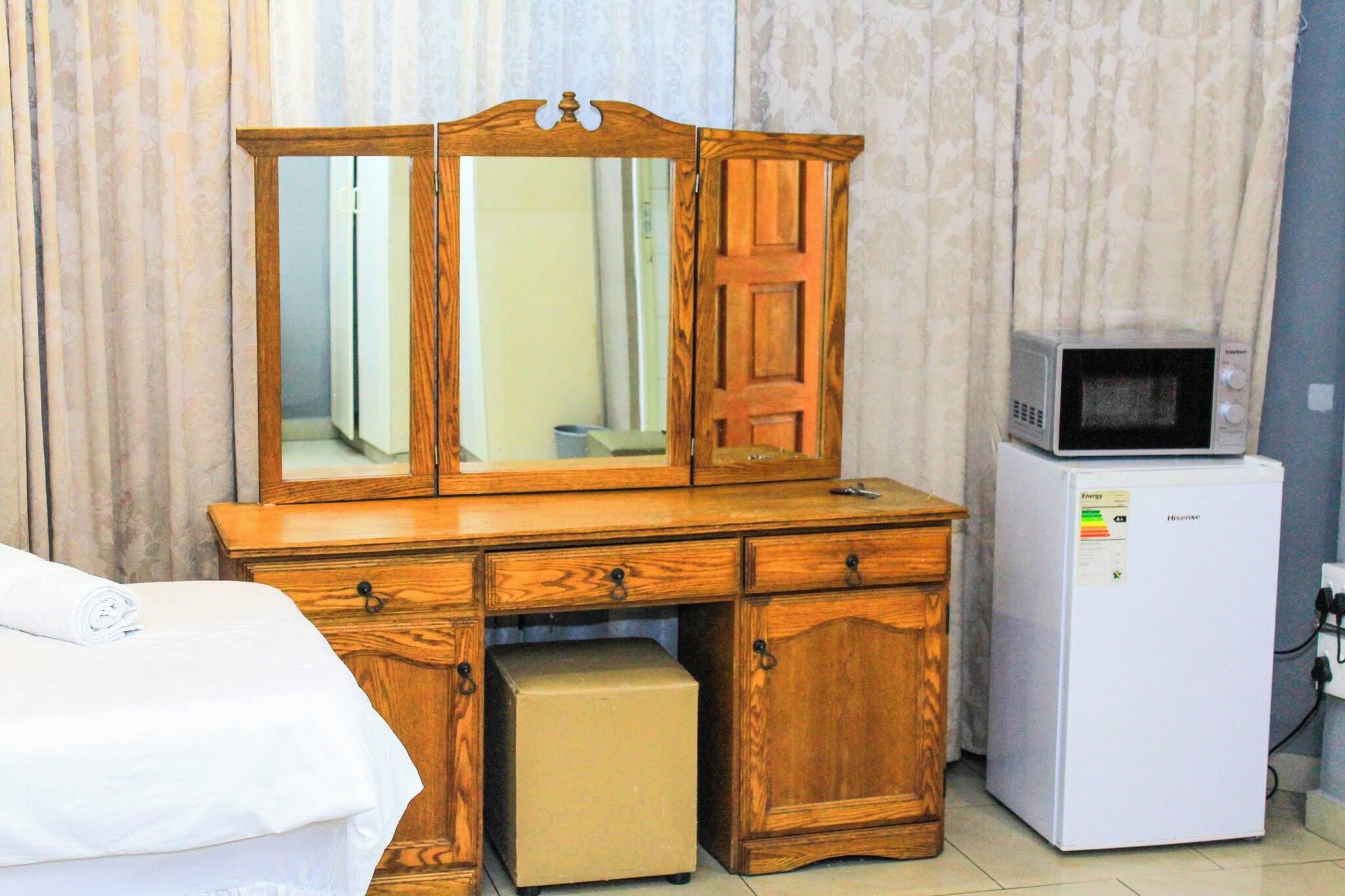 Dans une chambre d’hôtel, on trouve une commode en bois avec un miroir, un four à micro-ondes et un petit réfrigérateur.