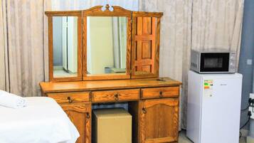 Dans une chambre d’hôtel, on trouve une commode en bois avec un miroir, un four à micro-ondes et un petit réfrigérateur.