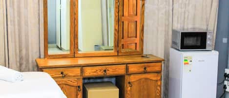 A wooden dresser with a mirror, a microwave, and a small refrigerator in a hotel room.
