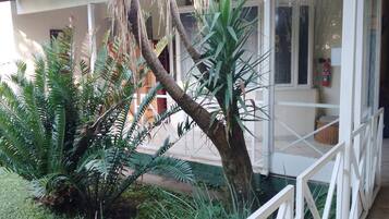 Un bâtiment à l’extérieur blanc, doté d’une porte en verre et d’un petit jardin agrémenté de diverses plantes.