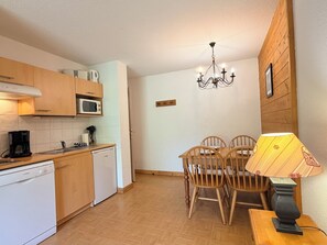 Cocina compacta con muebles de madera, microondas, lavavajillas Bosch y zona de comedor con mesa y sillas.