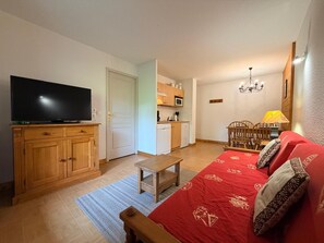 Un espacio habitable compacto con televisor, muebles de madera, un sofá rojo, una mesita y una kitchenette.