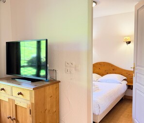 Ein Zimmer mit Fernseher auf einer Holzkassette, einem Bett mit weißer Bettwäsche und einer Steckdose.