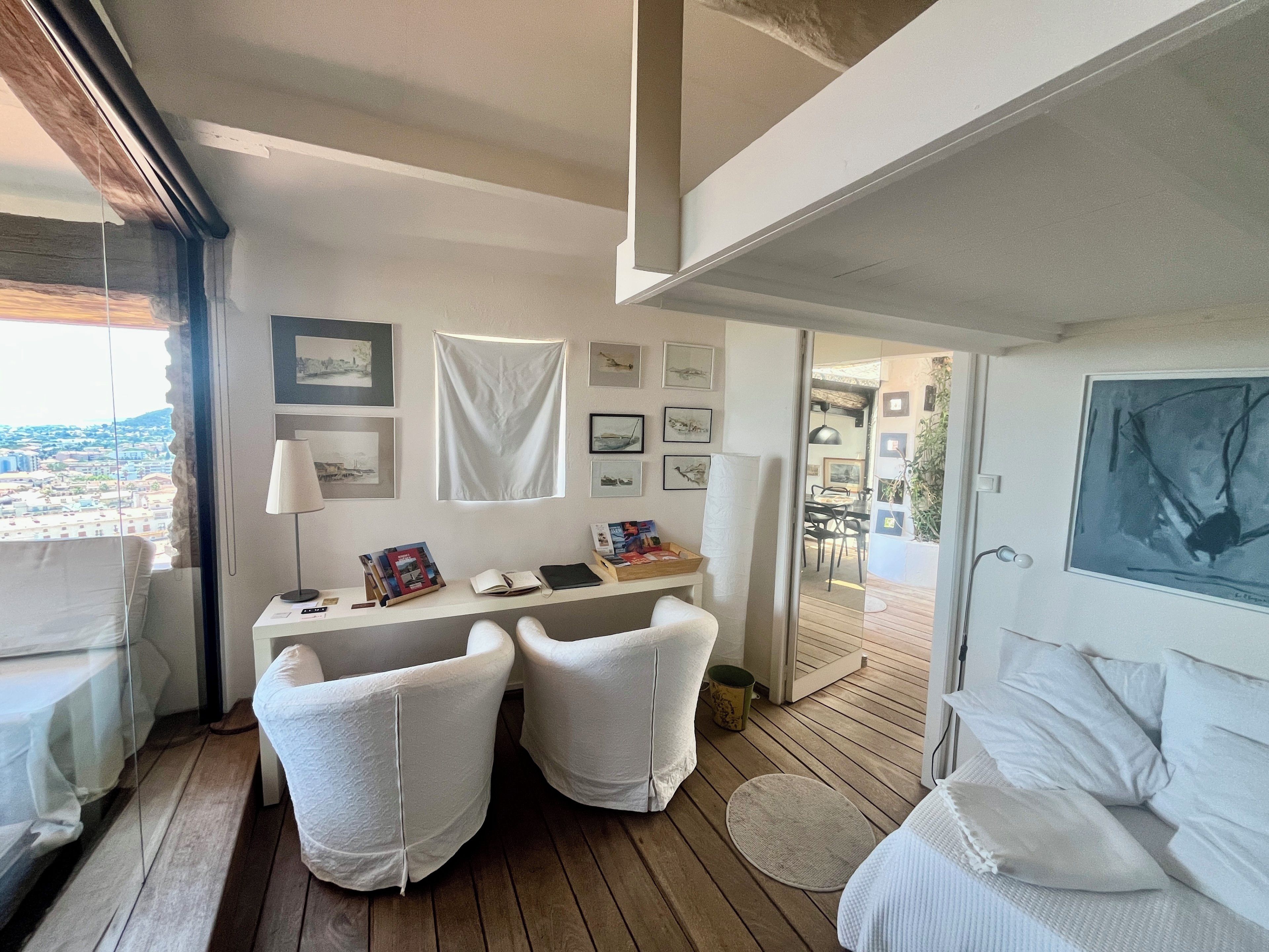A room with a desk, two chairs, a bed, and a view of the city.