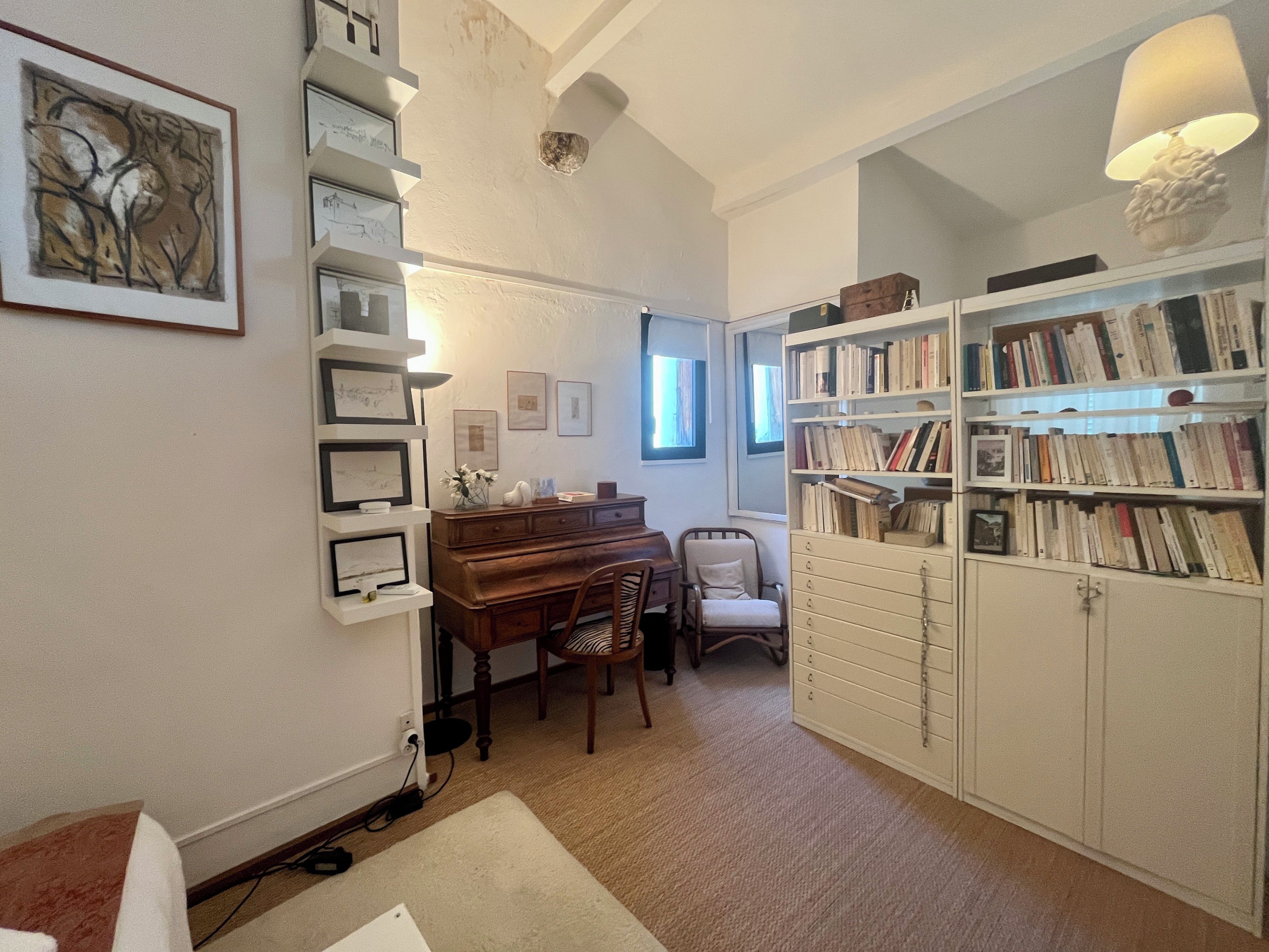 A room with a piano, a bookshelf, and a desk with a lamp.