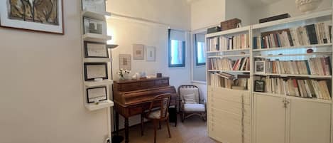 A room with a piano, a bookshelf, and a desk with a lamp.