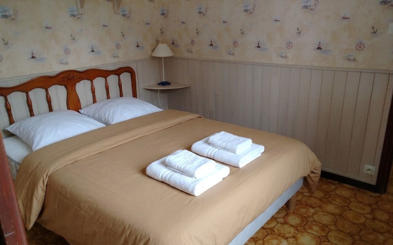 Una camera d'albergo con un letto, due cuscini, un comodino con una lampada e uno sfondo decorato.
