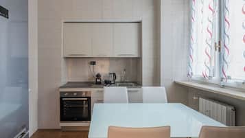 Eine moderne Küche mit weißen Schränken, einem eingebauten Backofen, einem Esstisch mit Stühlen und einem Fenster mit gemusterten Vorhängen.
