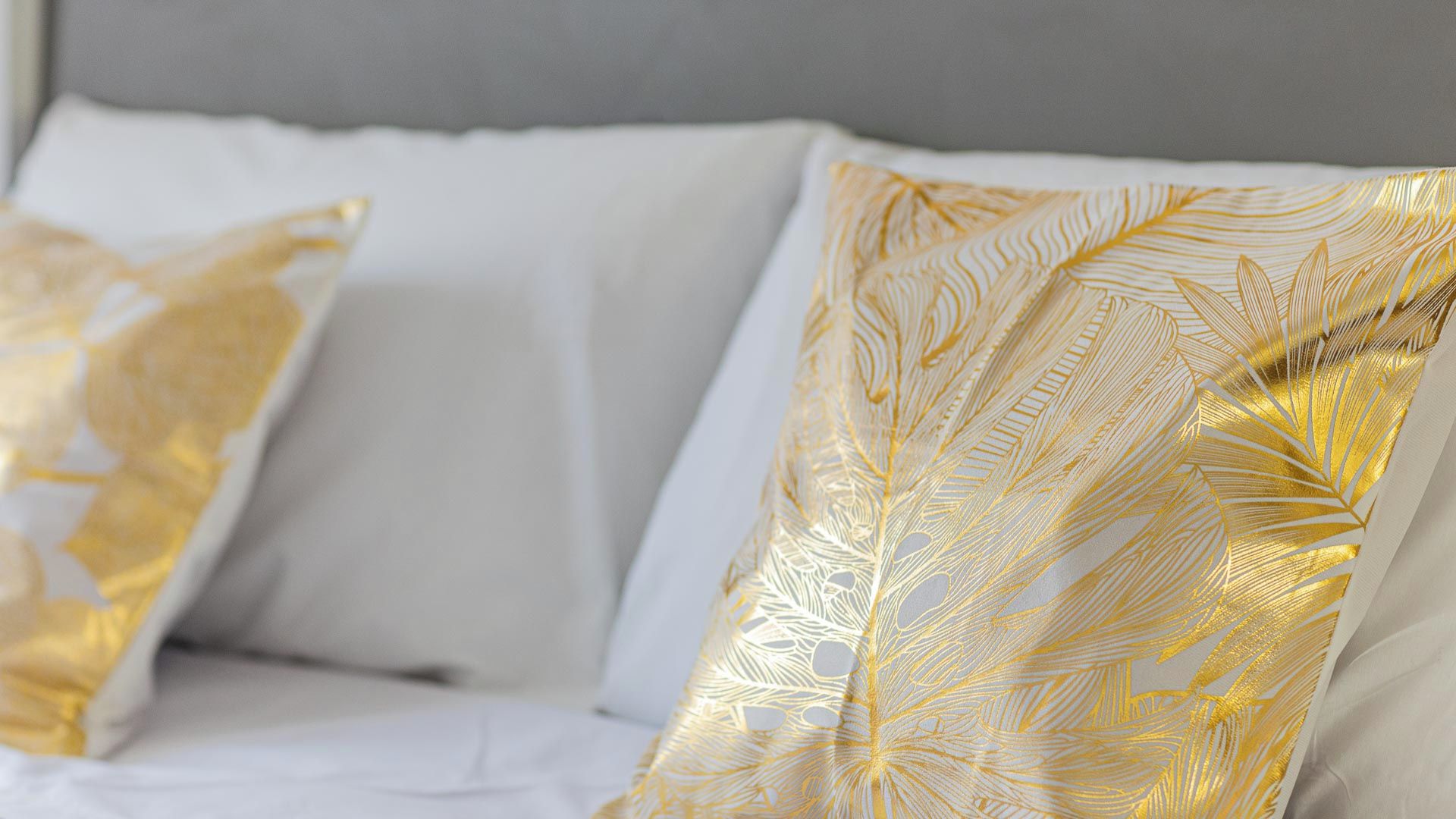 A bed with white bedding and decorative pillows with gold leaf patterns.