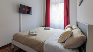 Une chambre d’hôtel avec un lit, un téléviseur fixé au mur et une fenêtre avec des rideaux rouges.