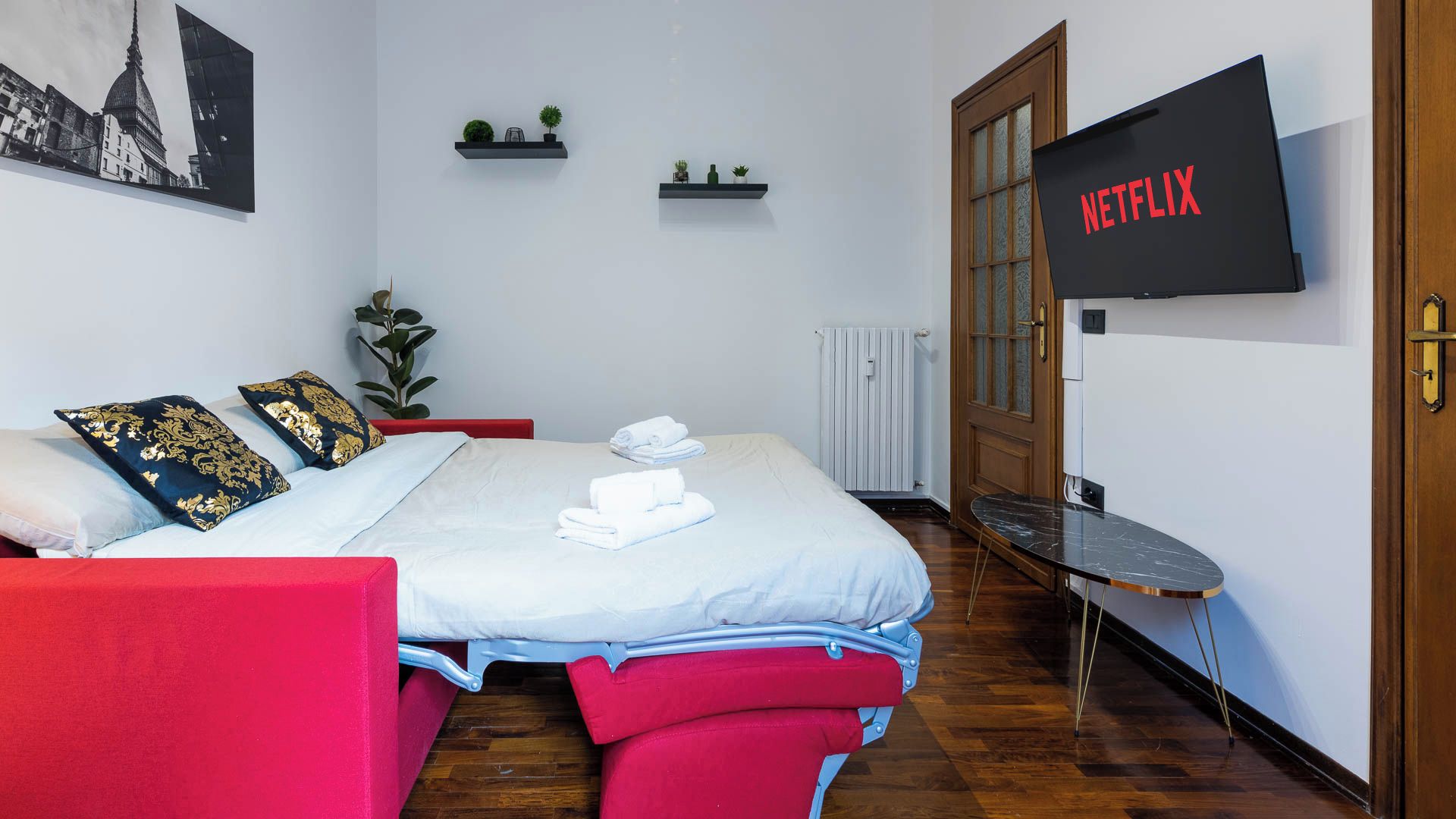 Ein Hotelzimmer mit einem Bett, einem roten Sessel, einem an der Wand montierten Fernseher und einer Tür mit Holzrahmen.