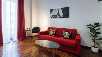 Ein modernes Wohnzimmer mit einem roten Sofa, zwei Zierkissen, einem Marmor-Couchtisch, einem schwarzen Sessel, einem kleinen Beistelltisch und einer Topfpflanze.