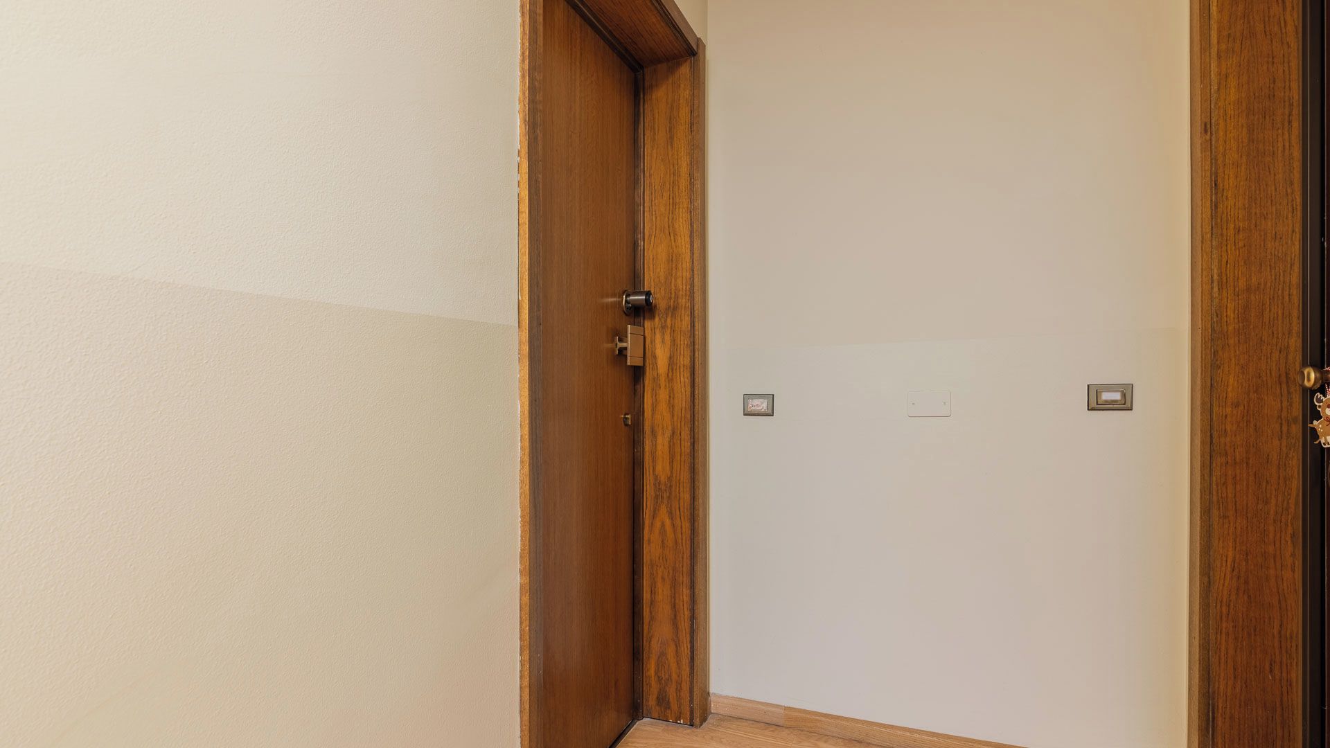 Ein Flur mit einer Holztür, einem Lichtschalter und einem kleinen Bilderrahmen an der Wand.