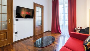 Un salon moderne avec un téléviseur à écran plat affichant le logo de Netflix, une porte en bois, un canapé rouge et une table basse en marbre.