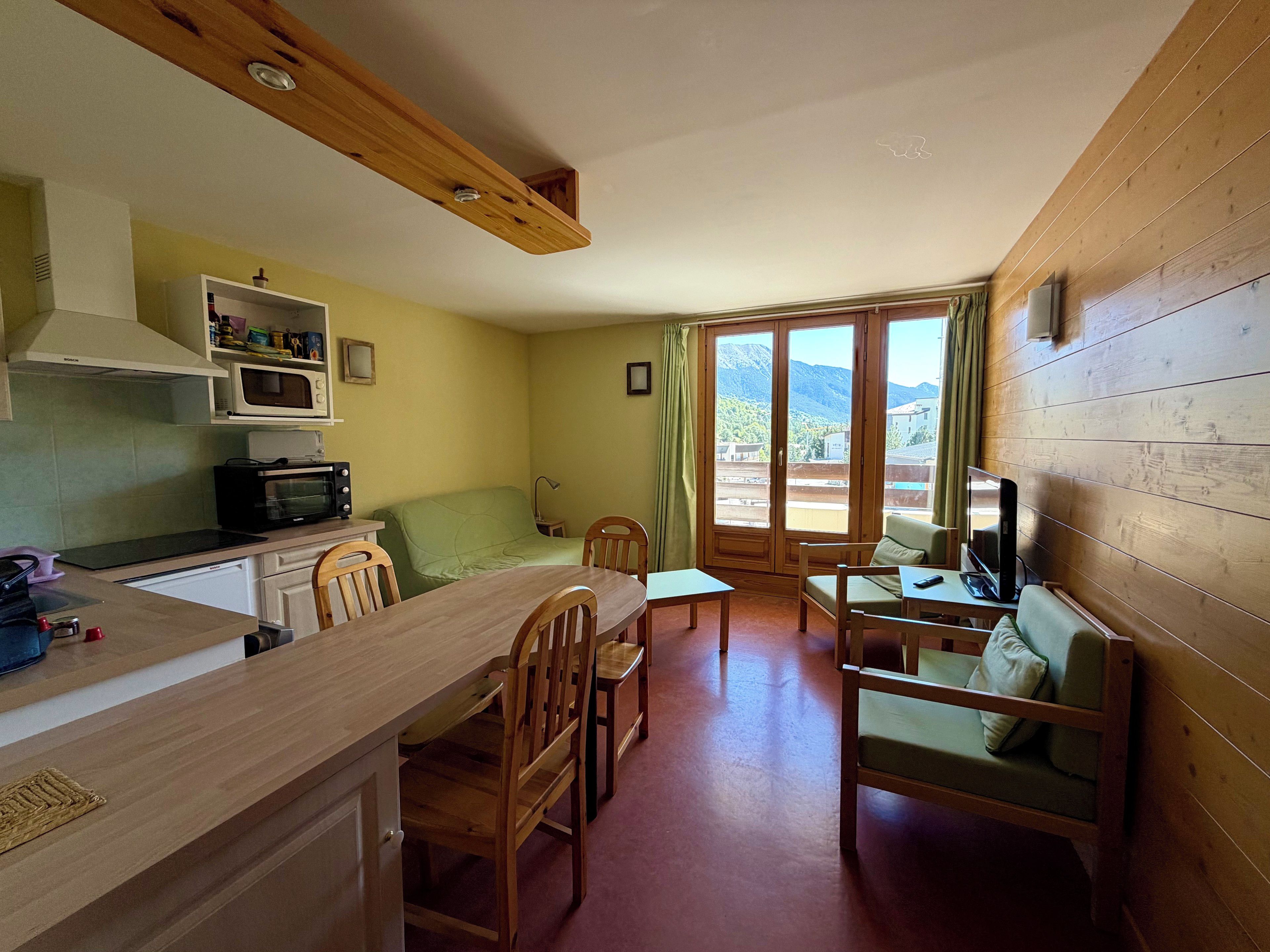 Un espace de vie compact comprenant une cuisine, un coin repas et offrant une vue sur les montagnes grâce à de grandes fenêtres.
