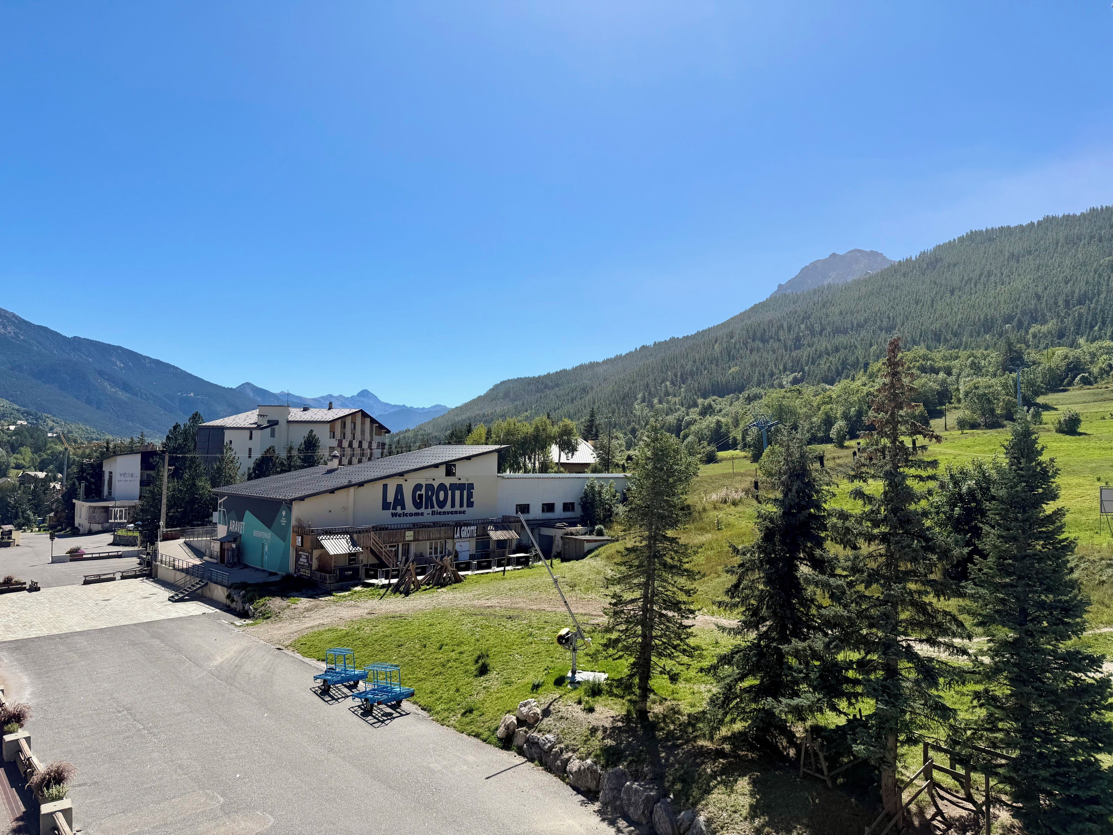 A building with 'LA GROTTE Welcome - Bienvenue' signage, surrounded by a mountainous landscape.