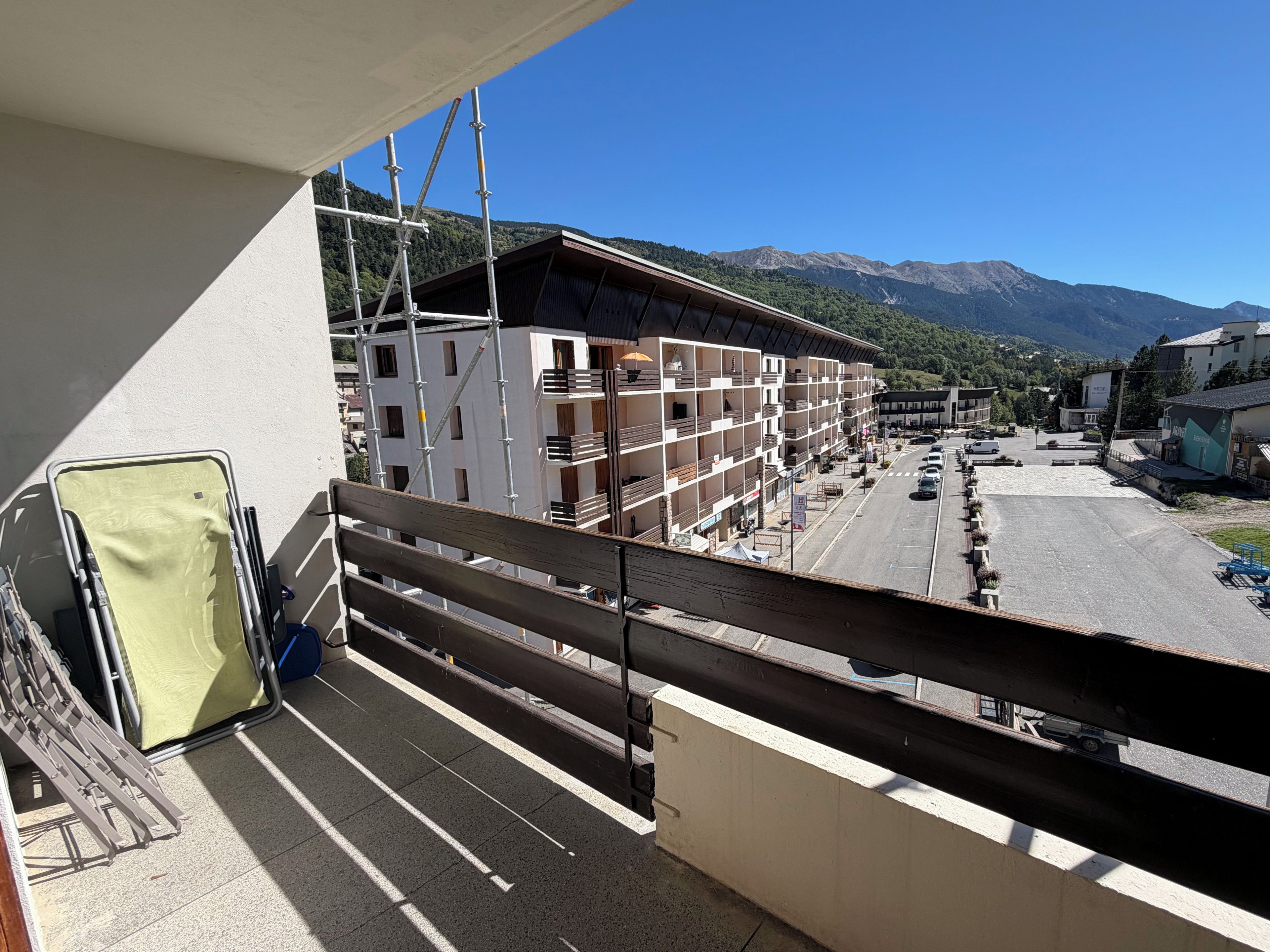 A balcony with a view of a building under construction, a parking lot, and mountains in the background.