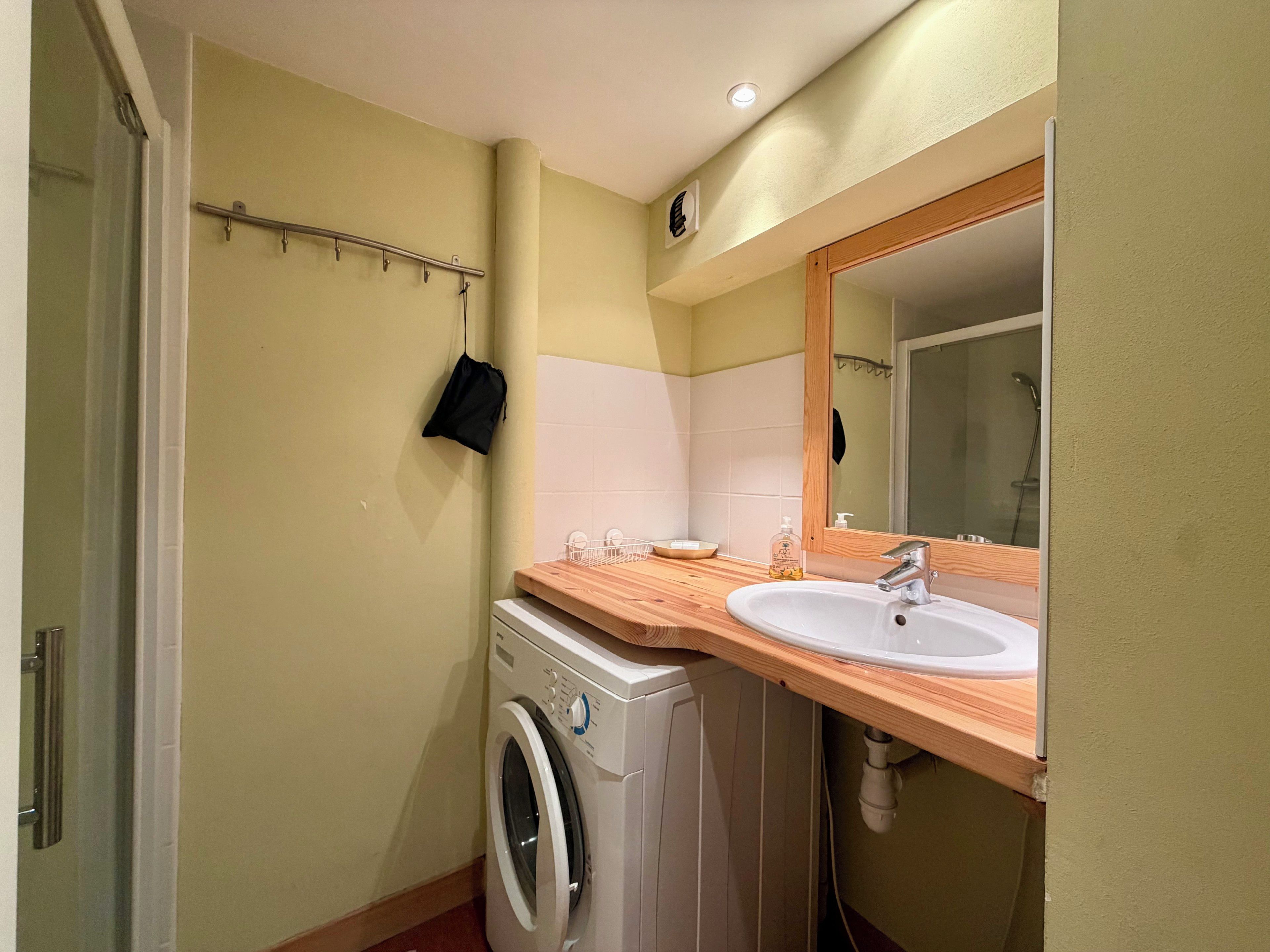A compact bathroom with a washing machine, a sink, and a mirror.