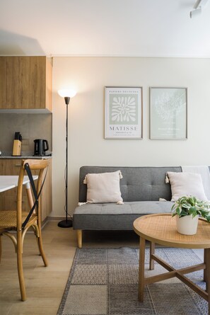 Ein modernes Wohnzimmer mit einem grauen Sofa, einem Holzstuhl, einer Stehlampe und zwei gerahmten Kunstwerken an der Wand.