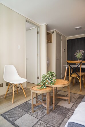 A hotel room with a bed, a dining table with chairs, a white chair, a small table with a plant, and a fan. - Sleek Santiago Retreat City Views for 3 (Santiago)