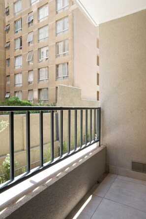 Ein Balkon mit Metallgeländer, einer beigen Wand und Blick auf ein mehrgeschossiges Gebäude mit Fenstern.