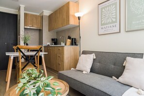 A modern living room with a grey sofa, wooden dining table, and chairs, a kitchen with wooden cabinets, and a framed artwork on the wall. - Sleek Santiago Retreat City Views for 3 (Santiago)