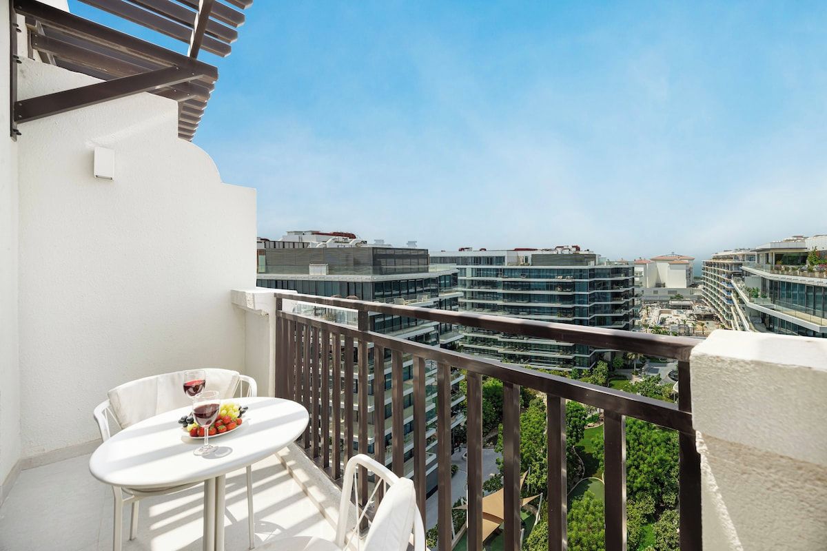 A balcony with a table and chairs, overlooking a modern urban area with multiple buildings.