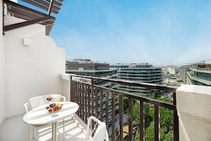 Een balkon met een tafel en stoelen, met uitzicht op een modern stedelijk gebied met meerdere gebouwen.
