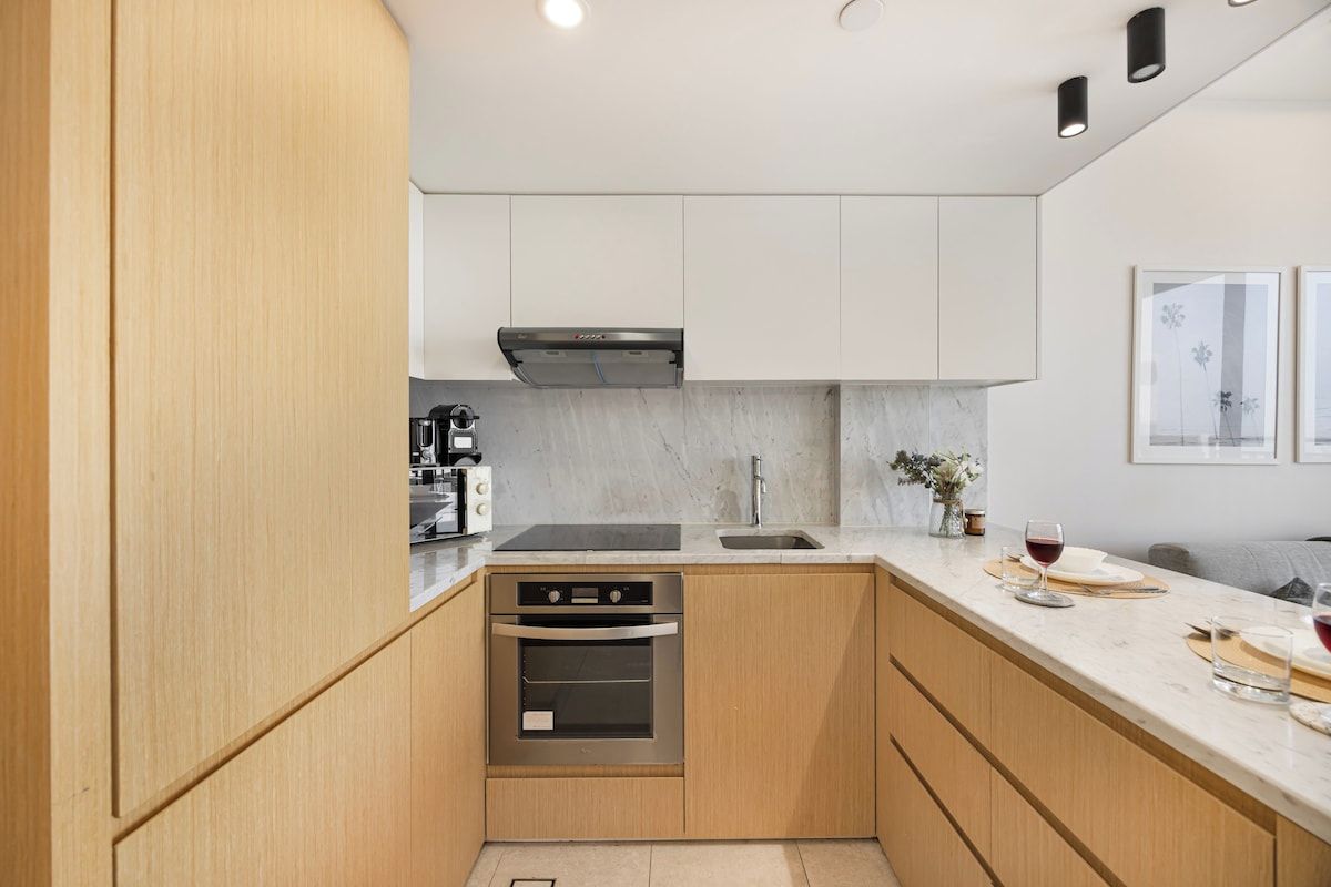 A modern kitchen with wooden cabinets, a stainless steel oven, a marble countertop, and a sink.