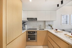 Een moderne keuken met houten kastjes, een roestvrijstalen oven, een marmeren aanrechtblad en een spoelbak.