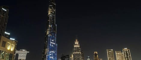 A nighttime cityscape with a prominent skyscraper, a waterfront with a fountain, and surrounding high-rise buildings.