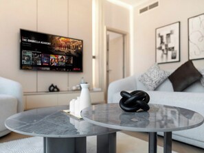 Uma sala de estar moderna com uma mesa de centro redonda de vidro, uma TV de tela plana na parede, um sofá branco e arte abstrata nas paredes.