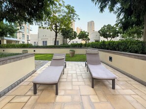 A patio area with two lounge chairs and a small table, surrounded by a low wall and greenery. - Full Burj Khalifa & Fountain Views/ Opp Dubai Mall (Dubai)