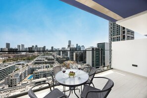 A balcony with a table and chairs, a city view, and a clear sky. - City Views / Pool & Gym / Near Circle Mall JVC (Dubai)