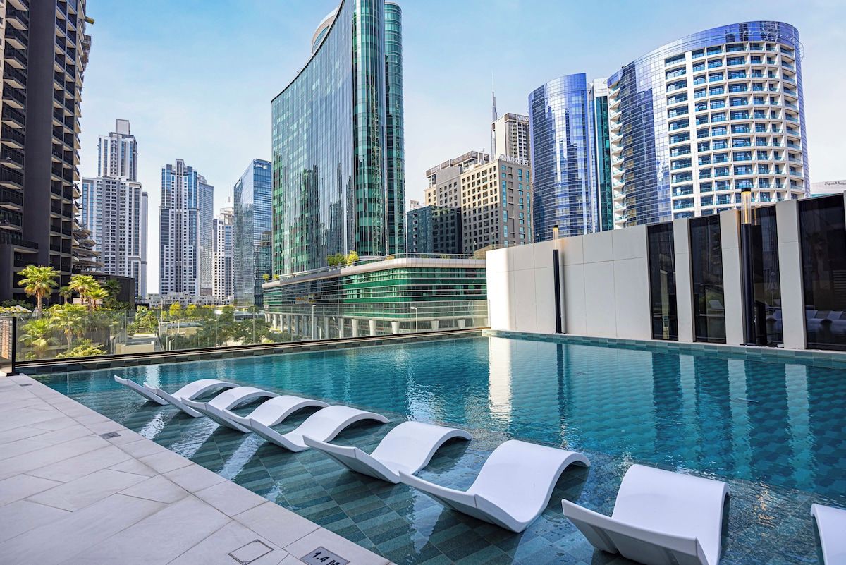 A modern hotel pool with lounge chairs, surrounded by high-rise buildings.
