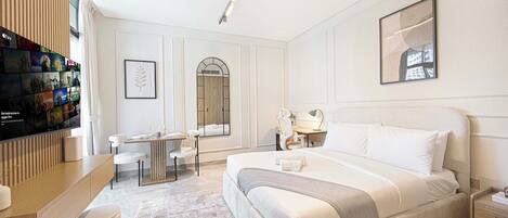 Une chambre d’hôtel avec un grand lit, un bureau avec une chaise, une télévision et une étagère murale remplie de livres.