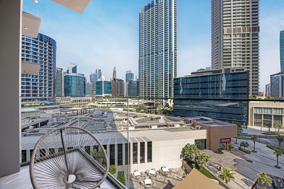 Un hotel moderno urbano con terraza en la azotea, edificios altos al fondo y cielo despejado.