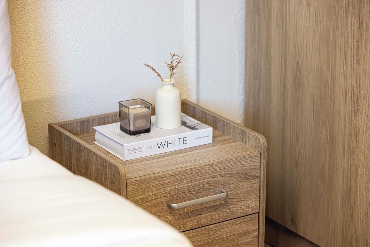 Ein Nachttisch aus Holz mit einer weißen Vase und einem Buch mit dem Titel 'WHITE'.