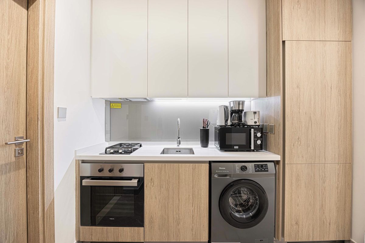 A compact kitchen with a built-in oven, microwave, coffee maker, and washing machine.