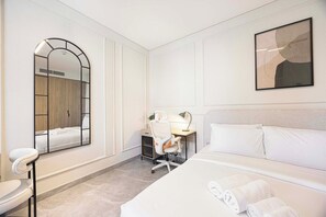 Quarto de hotel com cama, escrivaninha, cadeira, espelho e quadro na parede.